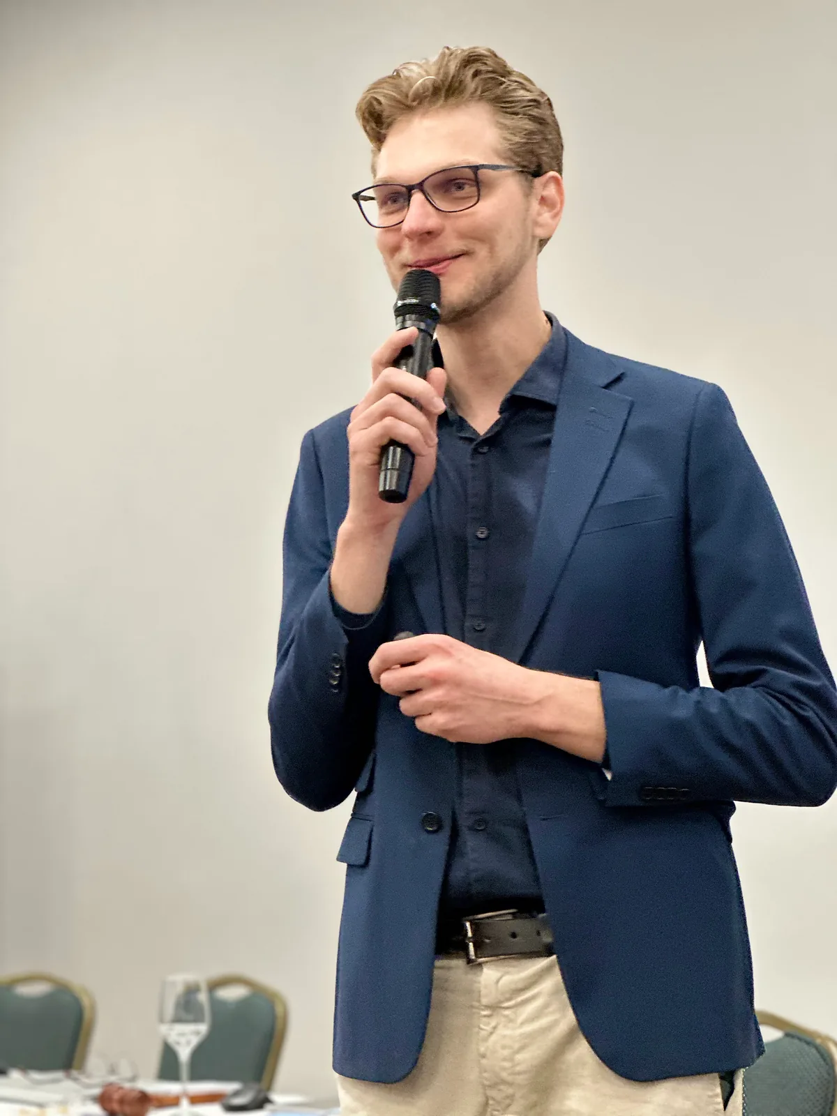Ricardo Werlang sorrindo ao microfone, blazer azul-marinho, na palestra do Senado JCI.