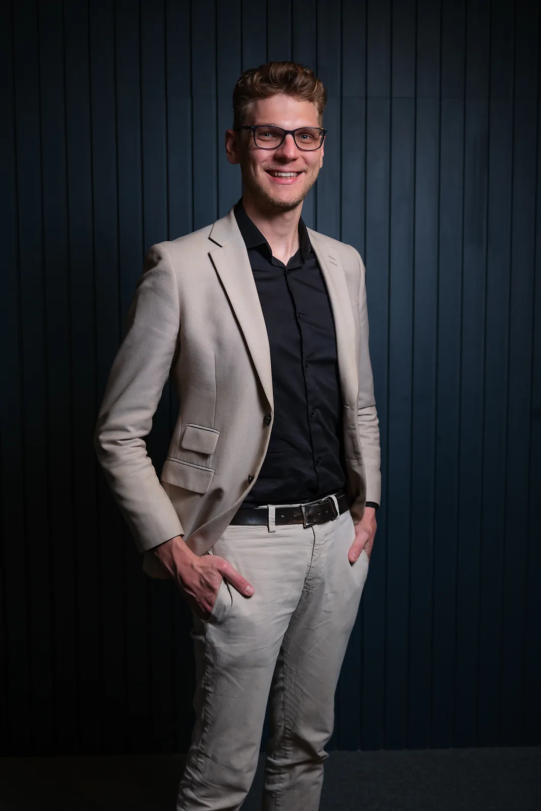 Ricardo Werlang de blazer bege e camisa preta, fundo azul-marinho.