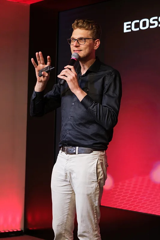 Ricardo Werlang em palestra, microfone na mão, telão vermelho, Expert Experience, 2025.