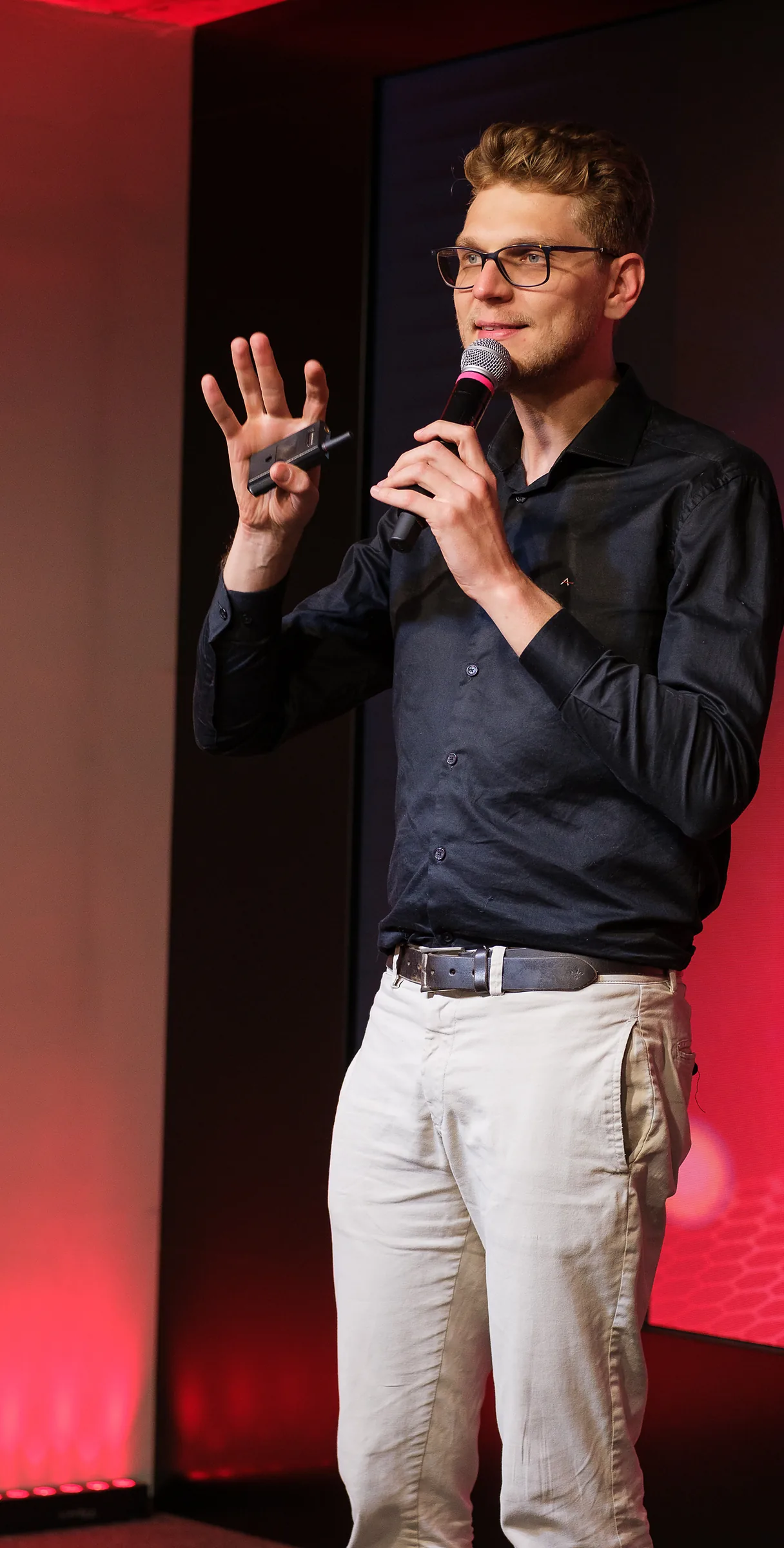 Ricardo Werlang em palestra no Expert Experience, microfone na mão, telão vermelho ao fundo.